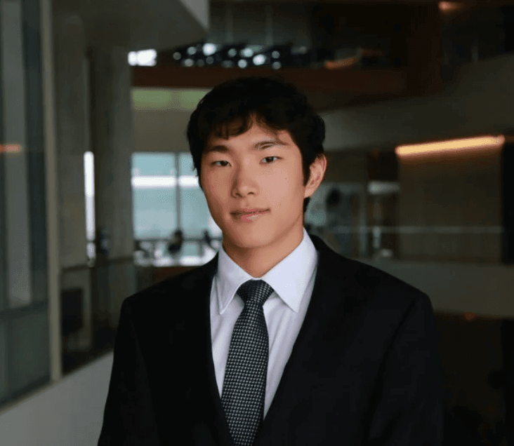 Young man in a suit and tie standing in an office hallway.